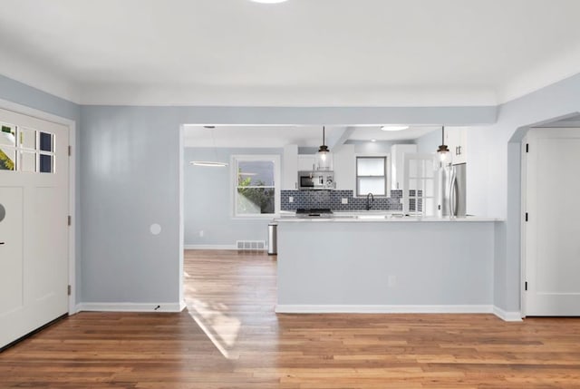 kitchen featuring kitchen peninsula, hanging light fixtures, white cabinetry, hardwood / wood-style floors, and stainless steel appliances