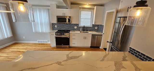 kitchen featuring white cabinets, appliances with stainless steel finishes, sink, backsplash, and hanging light fixtures