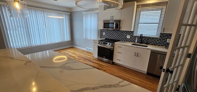 kitchen with appliances with stainless steel finishes, sink, decorative light fixtures, tasteful backsplash, and white cabinetry