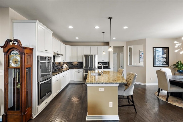 kitchen with sink, white cabinetry, hanging light fixtures, dark stone countertops, and stainless steel appliances