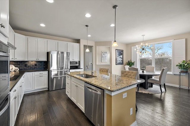 kitchen featuring pendant lighting, sink, white cabinets, stainless steel appliances, and a center island with sink