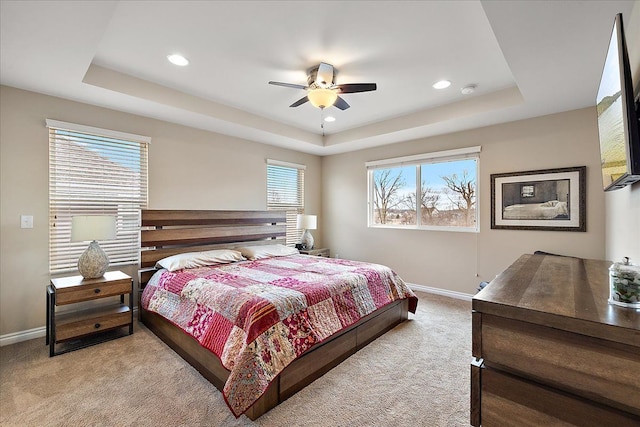 bedroom with light colored carpet, a raised ceiling, and ceiling fan