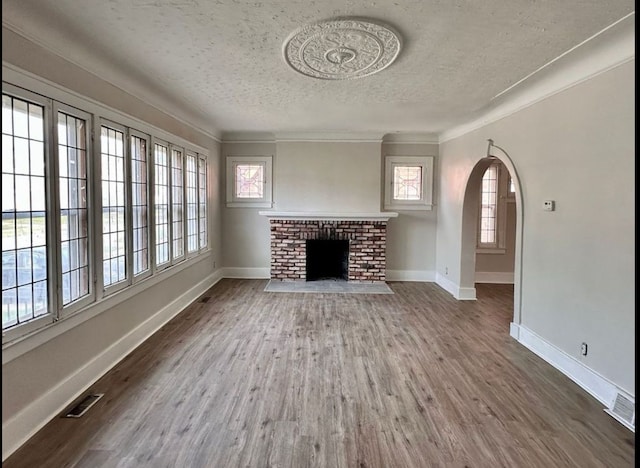 unfurnished living room featuring a brick fireplace, ornamental molding, dark wood-type flooring, and a textured ceiling