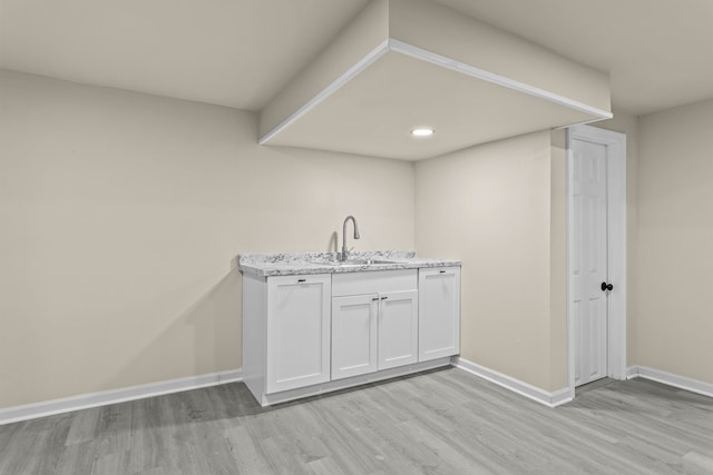 interior space featuring sink, white cabinetry, light stone countertops, and light hardwood / wood-style floors