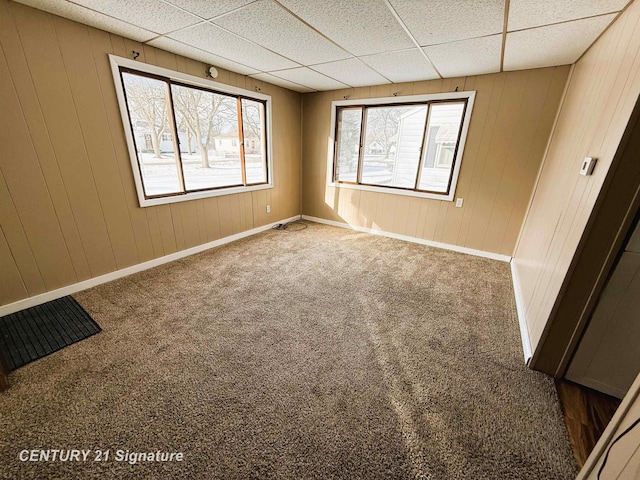 empty room featuring carpet, wood walls, and a drop ceiling