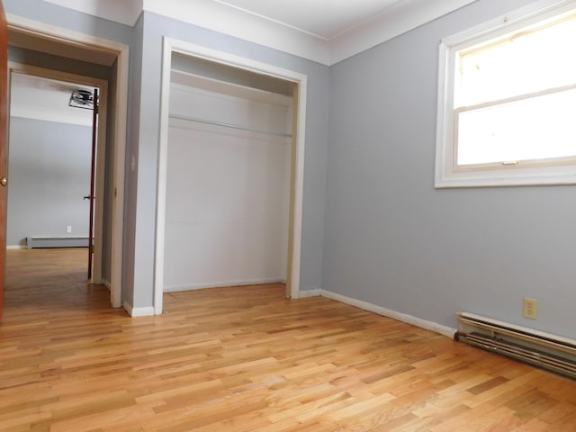 unfurnished bedroom with a closet, a baseboard heating unit, and light hardwood / wood-style flooring