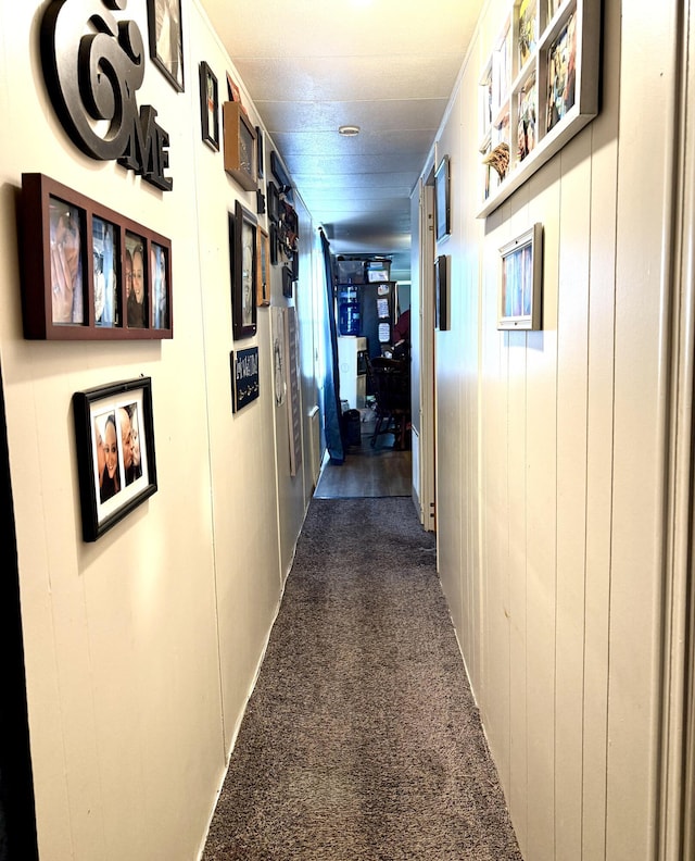 corridor featuring dark carpet and wood walls