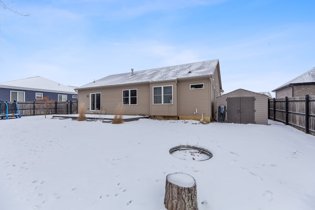 snow covered back of property with a trampoline and a shed