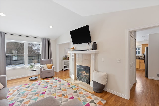 living room with a tiled fireplace, light hardwood / wood-style floors, and lofted ceiling