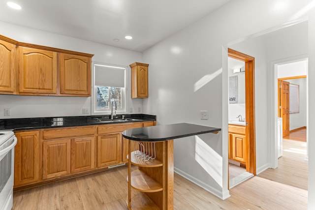 kitchen featuring white electric range oven, dark stone countertops, light hardwood / wood-style floors, and sink