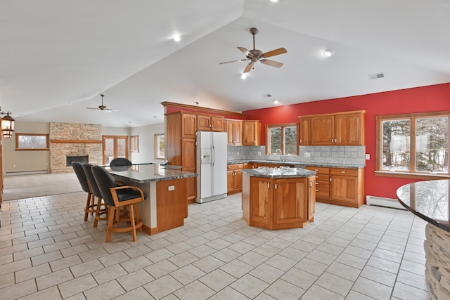 kitchen featuring white fridge with ice dispenser, lofted ceiling, a kitchen island, a baseboard heating unit, and decorative backsplash