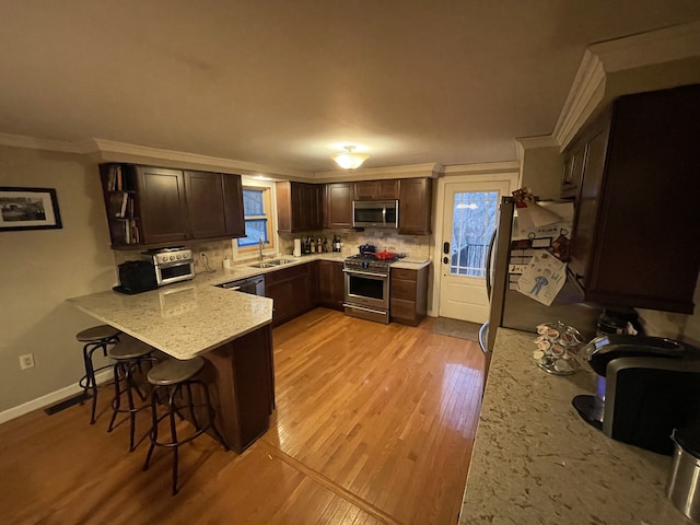 kitchen featuring a kitchen bar, appliances with stainless steel finishes, sink, kitchen peninsula, and ornamental molding