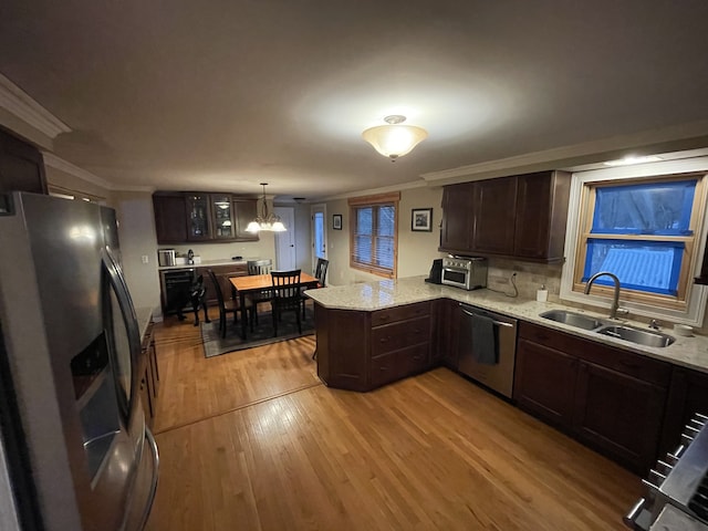 kitchen with glass insert cabinets, a peninsula, hanging light fixtures, stainless steel appliances, and a sink