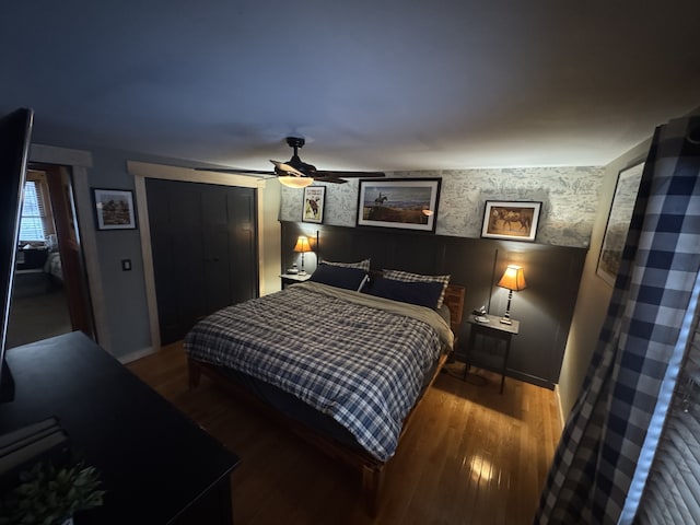 bedroom featuring a ceiling fan, wallpapered walls, baseboards, and wood finished floors