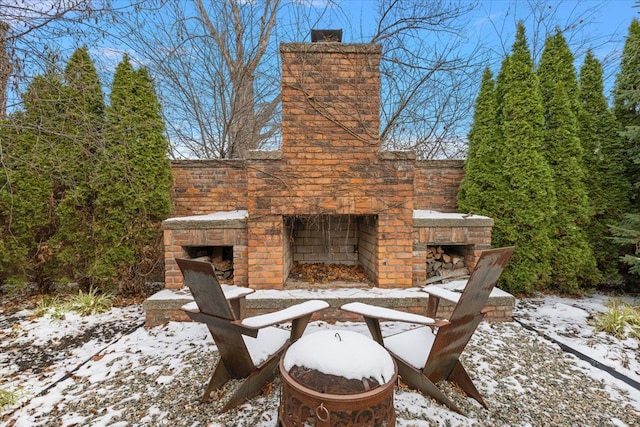 snow covered patio featuring an outdoor stone fireplace