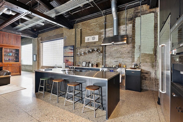 kitchen with high end stainless steel range oven, brick wall, sink, and an island with sink