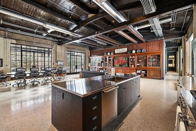 kitchen featuring wooden walls, sink, a kitchen island with sink, stainless steel dishwasher, and dark brown cabinets