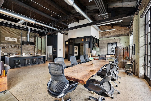 home office with beamed ceiling, a towering ceiling, and brick wall