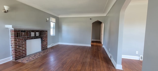 unfurnished living room featuring a brick fireplace and dark wood-type flooring