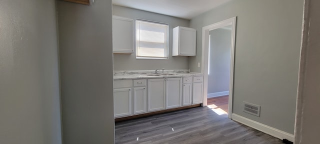 kitchen with sink, light stone counters, white cabinets, and light hardwood / wood-style floors