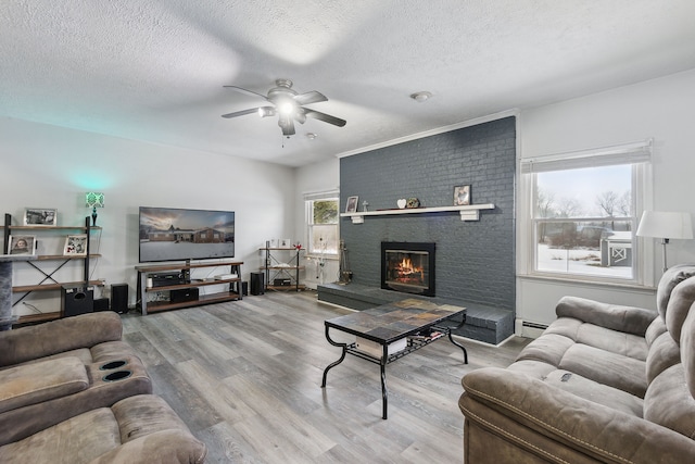 living room with wood-type flooring, a brick fireplace, a textured ceiling, baseboard heating, and ceiling fan