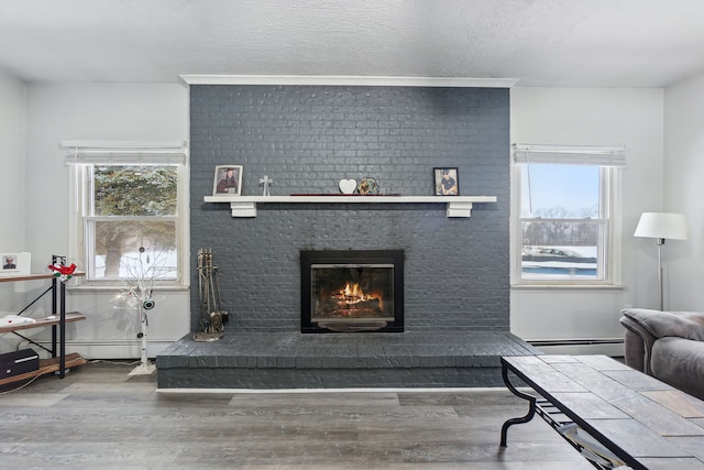 living room featuring hardwood / wood-style flooring, a baseboard heating unit, a brick fireplace, and a textured ceiling