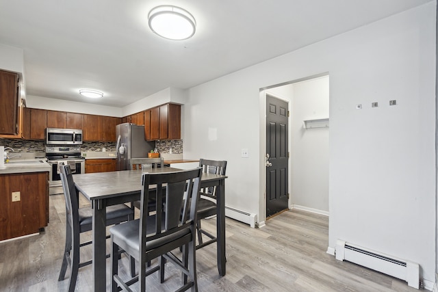 kitchen featuring sink, baseboard heating, appliances with stainless steel finishes, decorative backsplash, and light wood-type flooring