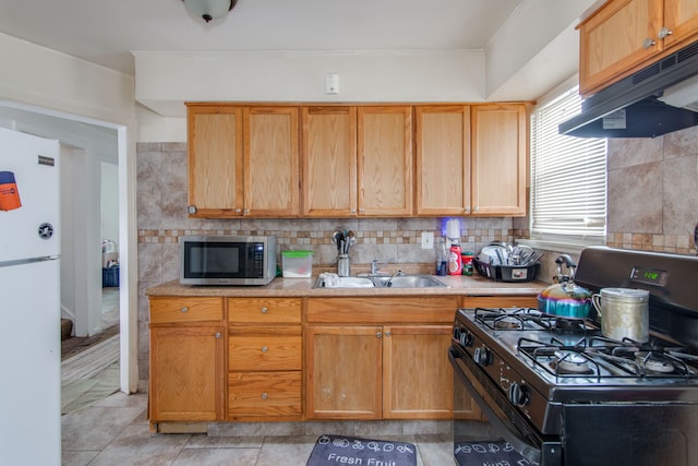 kitchen featuring range hood, white fridge, decorative backsplash, sink, and black range with gas stovetop