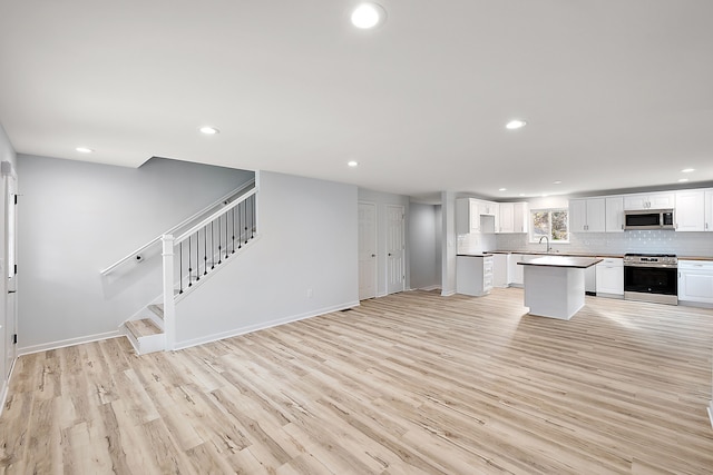 kitchen with appliances with stainless steel finishes, light wood-style floors, white cabinets, and decorative backsplash