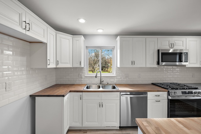 kitchen featuring stainless steel appliances, butcher block counters, white cabinetry, and a sink