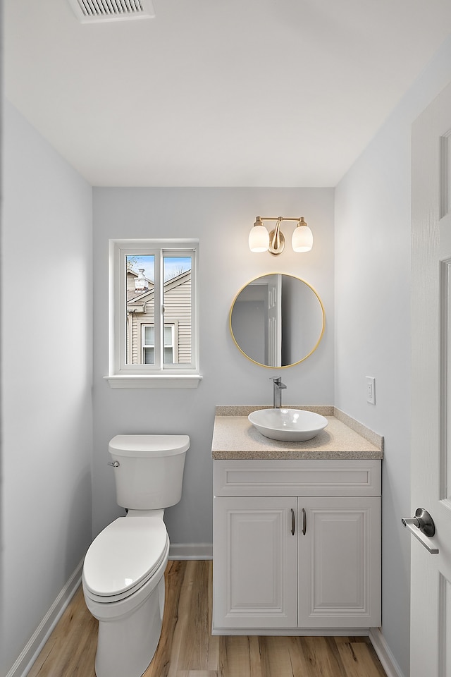 half bathroom featuring baseboards, visible vents, vanity, and toilet