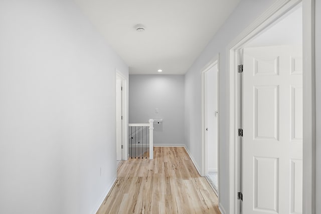 hall featuring light wood-type flooring, baseboards, and an upstairs landing