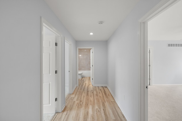 hallway featuring light wood-type flooring, baseboards, and visible vents