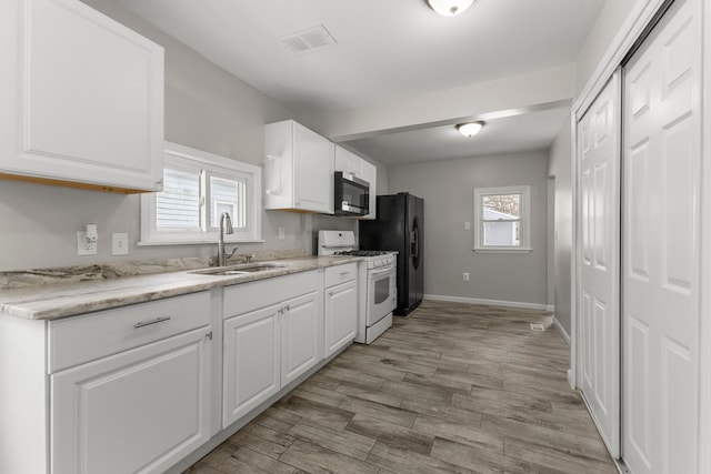 kitchen with sink, white cabinets, white gas range oven, light hardwood / wood-style floors, and black fridge