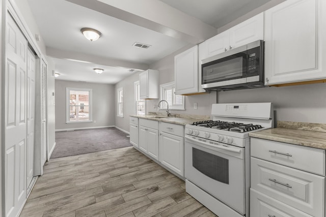 kitchen with light stone counters, sink, white cabinets, and gas range gas stove