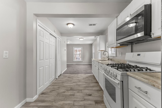 kitchen with white gas range oven, light stone countertops, white cabinetry, sink, and light hardwood / wood-style flooring