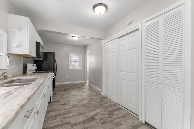 kitchen with white cabinets, white gas stove, light hardwood / wood-style flooring, and sink