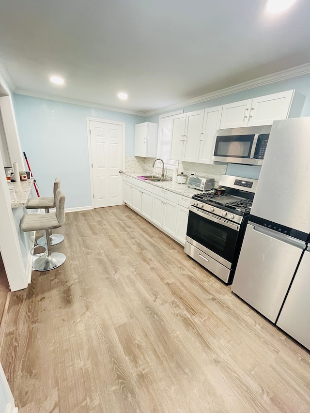 kitchen featuring white cabinetry, decorative backsplash, ornamental molding, light stone counters, and stainless steel appliances