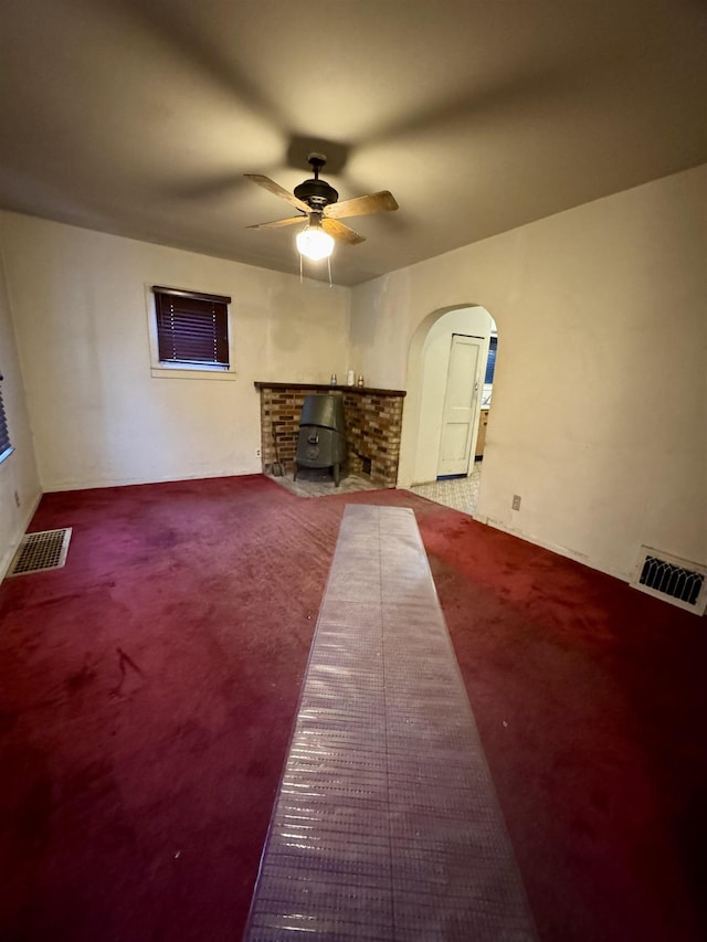 unfurnished living room with carpet floors, a wood stove, and ceiling fan