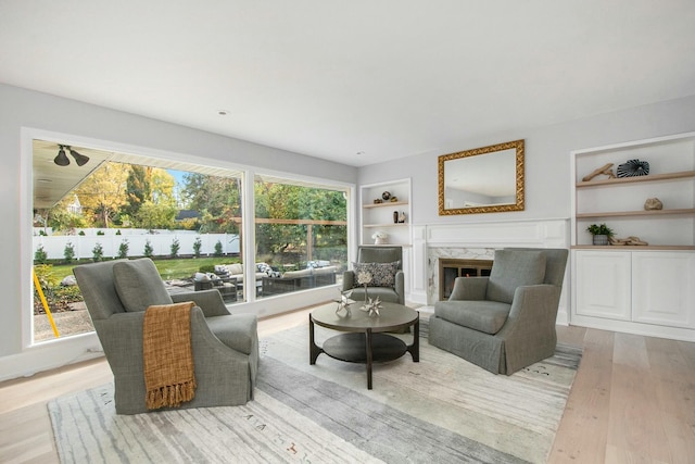 living room featuring light hardwood / wood-style floors, a high end fireplace, a wealth of natural light, and built in features