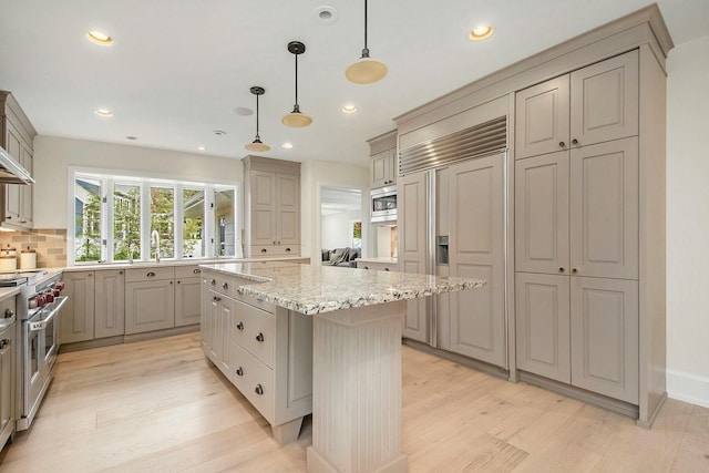 kitchen featuring pendant lighting, light stone countertops, a center island, decorative backsplash, and built in appliances