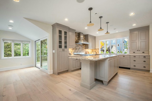 kitchen with pendant lighting, light hardwood / wood-style flooring, light stone countertops, wall chimney range hood, and a kitchen island