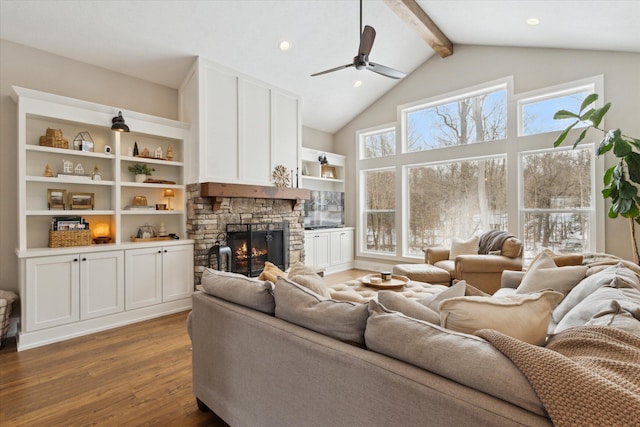 living room with dark wood-type flooring, beamed ceiling, plenty of natural light, and a stone fireplace