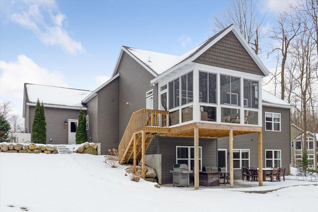 snow covered back of property with a sunroom