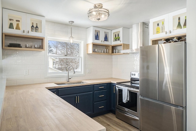 kitchen featuring wall chimney exhaust hood, stainless steel appliances, blue cabinetry, hanging light fixtures, and sink