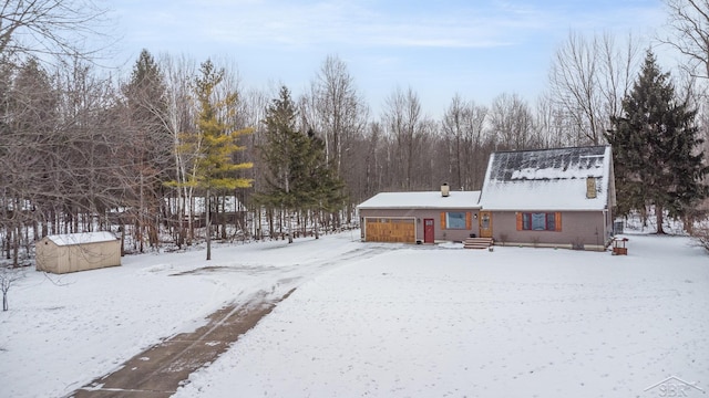 snow covered house featuring a garage, an outbuilding, and a storage unit