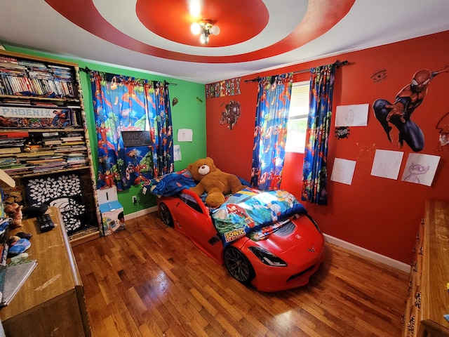 bedroom with wood-type flooring and a tray ceiling