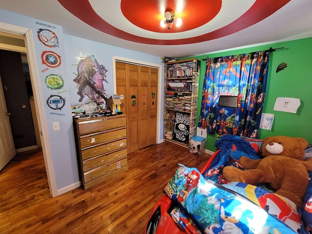 bedroom with a closet, dark hardwood / wood-style flooring, and a tray ceiling