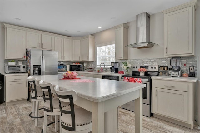 kitchen with a breakfast bar, light wood-type flooring, a kitchen island, stainless steel appliances, and wall chimney range hood