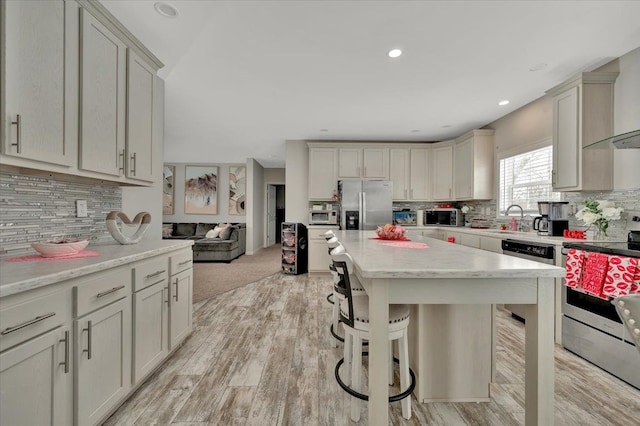 kitchen featuring a kitchen bar, appliances with stainless steel finishes, a kitchen island, light stone countertops, and wall chimney range hood